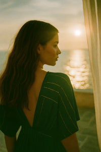 Woman in a green dress standing by a window with a sunset view